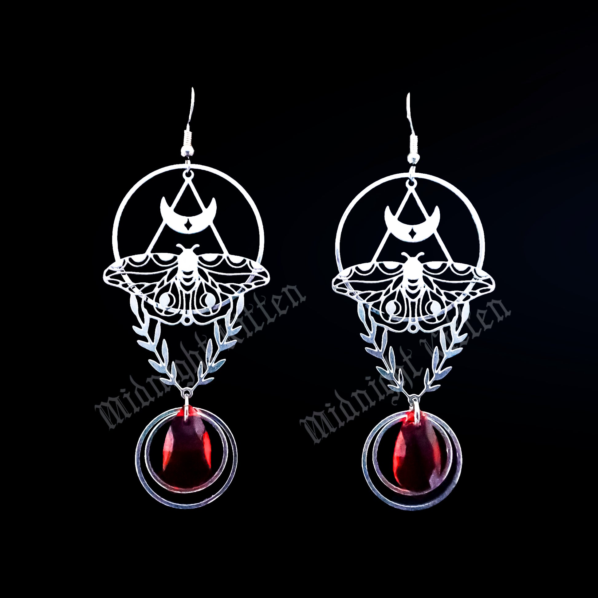 Pair of earrings with an intricate moth and laurel design and red stones on a black background