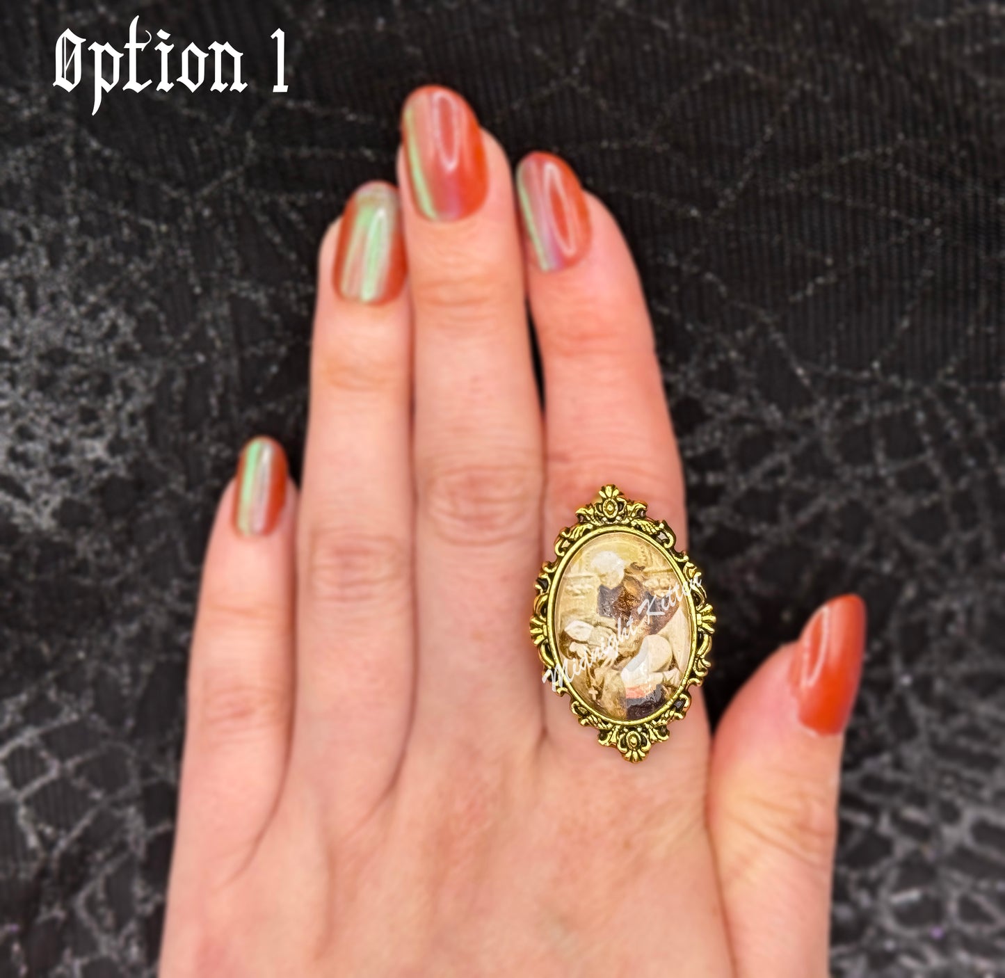 A gold ring with the decorative setting of a framed photograph on a hand against a textured black background. Option 1 contains a piece of Victorian-era pornography depicting a priest having intimate relations with a nun.